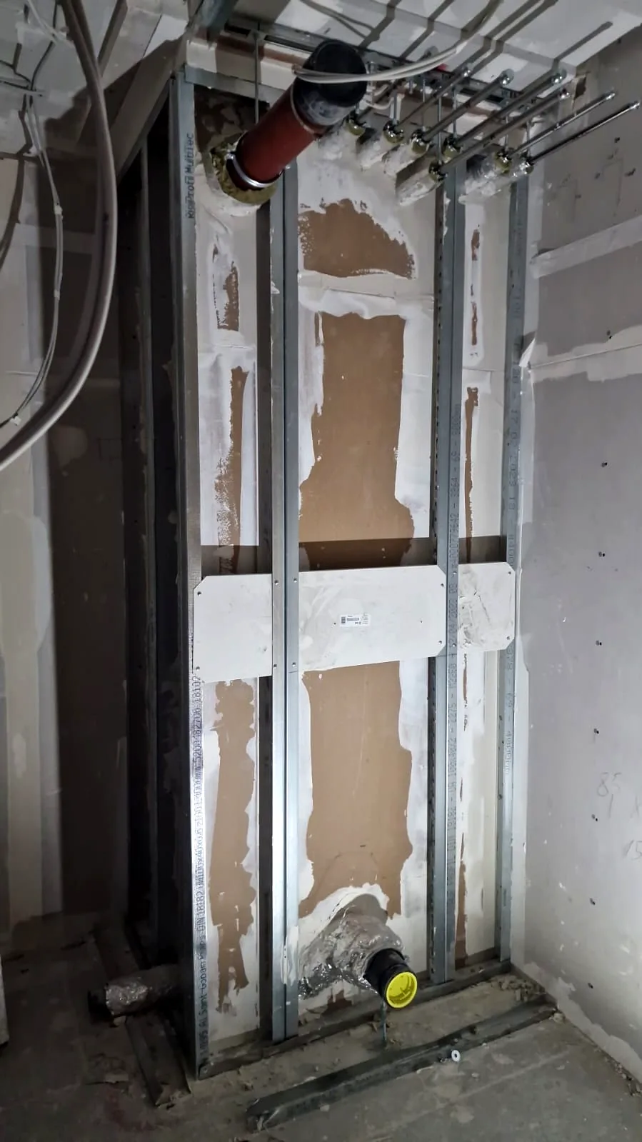 Ständerwerk eines Installationsschachts mit teilweise beplankter Gipskartonfläche und Abwasserleitung