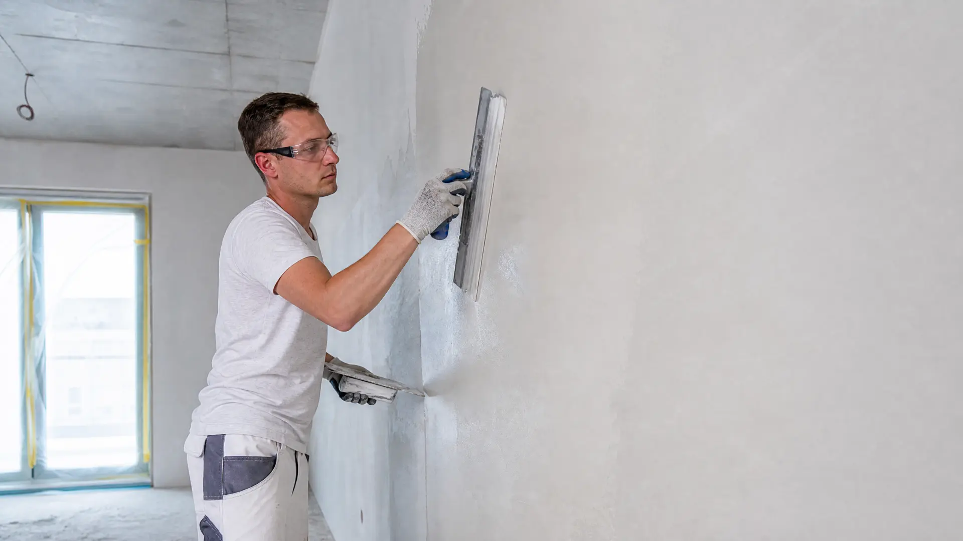 Handwerker zieht Flächenspachtel mit der Glättkelle auf einer Innenwand ab